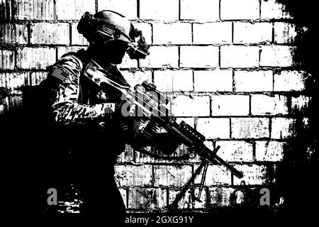 US Army Ranger member with machinegun and night vision goggles moving along the wall during mission Stock Photo