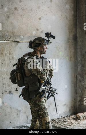 US Army Ranger with machinegun and night vision goggles standing near the wall. Side view profile Stock Photo
