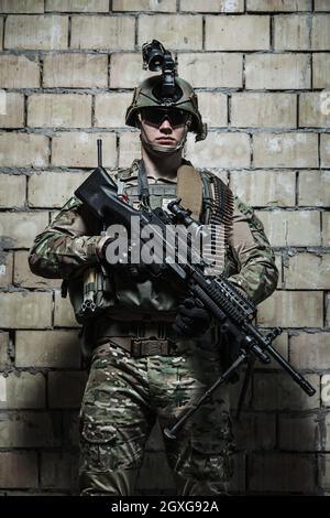 US Army Ranger with machinegun and night vision goggles standing near the wall. Front view portrait Stock Photo