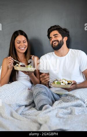 Healthy breakfast in bed. Young beautiful couple in love is sitting on bed and having breakfast. Stock Photo