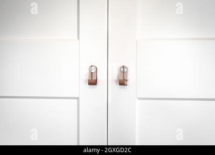 White wooden closet doors with retro brown leather handles wood closeup background texture of cupboard modern design Stock Photo