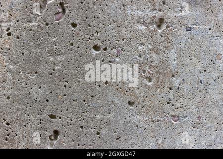 A flat grey concrete surface. The surface is textured and covered in holes from lots of tiny air bubbles. Stock Photo
