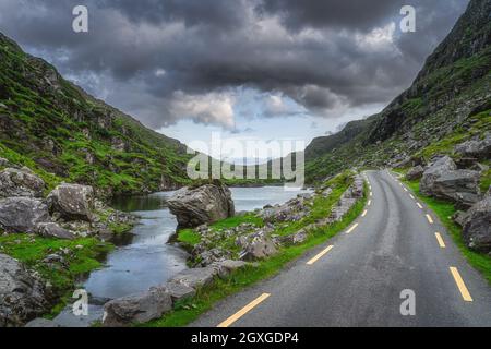 Winding road running through Gap of Dunloe with stone Wishing Bridge in distance, Black Valley, MacGillycuddys Reeks mountains, Ring of Kerry, Ireland Stock Photo