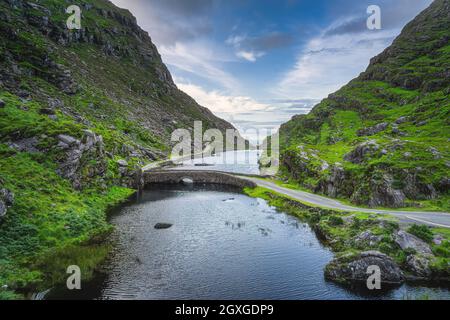 Winding narrow road crossing stone Wishing Bridge in Gap of Dunloe, Black Valley, MacGillycuddys Reeks mountains, Ring of Kerry, Ireland Stock Photo