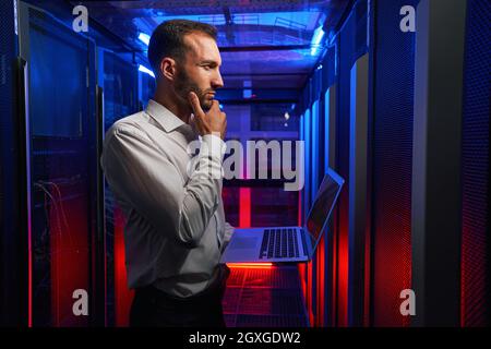 Bearded concentrated network engineer examining work of supercomputer in tech place Stock Photo
