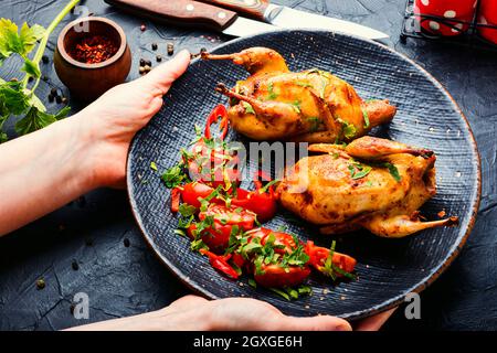 Baked whole quail and vegetable salad.Appetizing baked quail meat on plate in hands Stock Photo