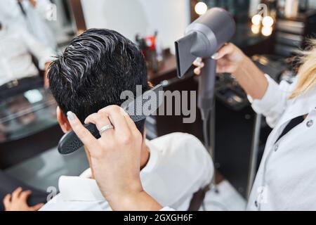 Specialist brushing hair on back of head while using hairdryer Stock Photo