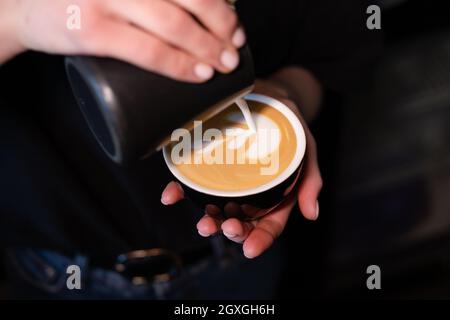 Barista pouring latte foam on coffee, espresso. creating a perfect latte art. dark colours, coffee house. Stock Photo