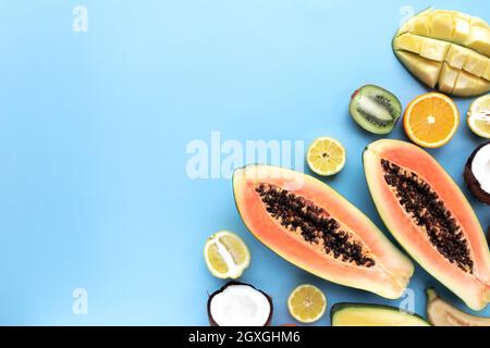 Different fresh tropical cut fruits on a blue background. Papaya, orange, banana, coconut, mango, kiwi and lemon top view flat lay with copy space for Stock Photo