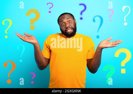 Confuse and pensive expression of a black boy with many questions . cyan colored background Stock Photo