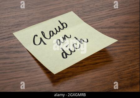 Sticky note with the text Believe in you in german - Glaub an dich Stock Photo