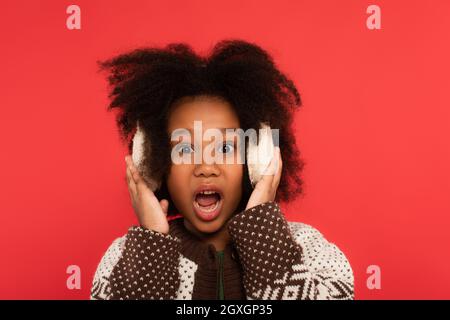 Amazed african american kid in ear muffs looking at camera isolated on red Stock Photo