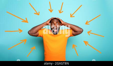 Feared, confused and shocked expression of a black boy followed by arrows. cyan colored background Stock Photo