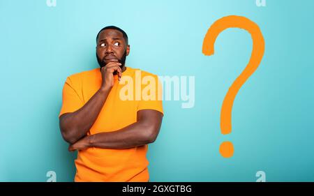 Confuse and pensive expression of a black boy with a big questions. cyan colored background Stock Photo