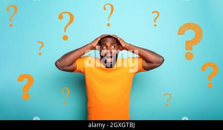 Feared and shocked expression of a black boy with many questions . cyan colored background Stock Photo