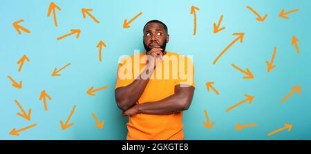 Confuse and pensive expression of a black boy with many arrows to follow . cyan colored background Stock Photo