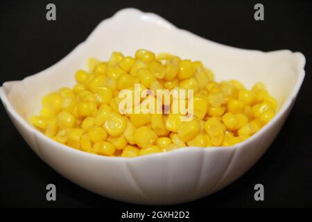 Canned sweet corn in white ceramic bowl isolated on black. Heap of corn kernels in plate close up. Food ingredients. Bowl with corn grains on black ba Stock Photo