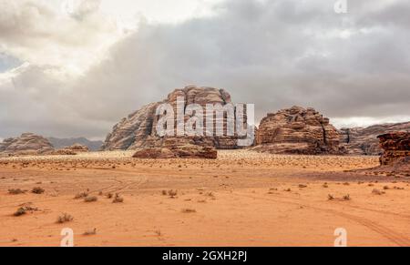 Rocky massifs on red orange sand desert, overcast sky in background - typical scenery in Wadi Rum, Jordan. Stock Photo