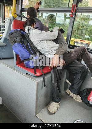 Homeless couple, young man and woman in dirty clothes with backpacks in public transport, sleeping on the bus. Unrecognizable people. Prague, Czech Republic - September 24, 2021 Stock Photo