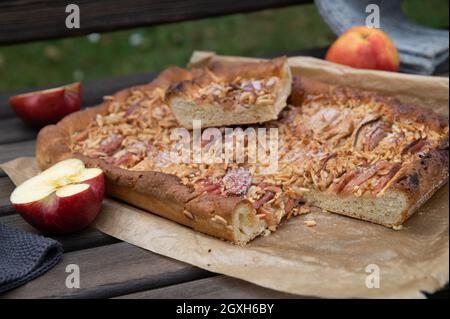 Fresh baked apple cake or apple pie with almonds served outside during autumn season on a wooden rustic bench. Stock Photo