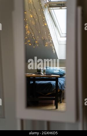 Reflection in mirror in home interior. Glass cup of hot water on table near bed Stock Photo