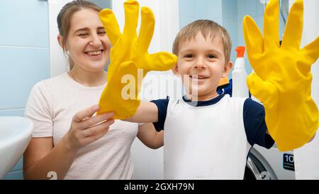 Funny laughing boy wearing yellow rubber gloves laughing and making faces before doing housewrok and cleaning bathroom with his mother. Family foing h Stock Photo