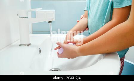 Closeup of yougn other washing her sons' hands with soap in bathroom sink. Concept of healthcare and hygiene. Stock Photo