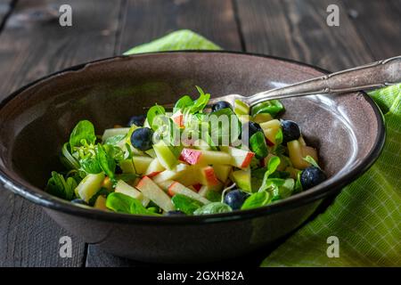 Organic fruit salad with lamb´s lattuce. Marinated with olive oil and apple cider vinegar. Served in a rustic brown enamel bowl on wooden table. Stock Photo