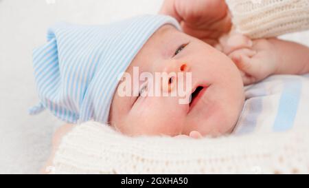 Closeup of caring mother dressign her newborn baby son and putting on blue hat. Concept of babies and newborn hygiene and healthcare. Caring parents w Stock Photo