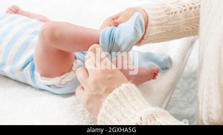 Closeup of mother putting on socks on her little baby son lying on changing table. Concept of babies and newborn hygiene and healthcare. Caring parent Stock Photo