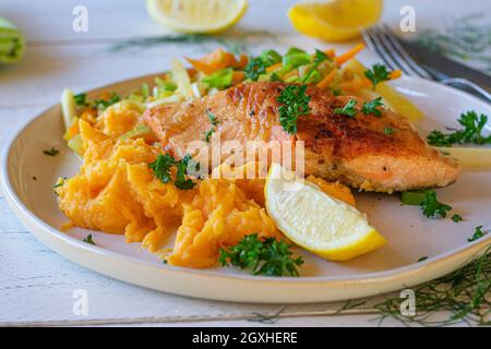 Dish with pan fried salmon fillet served with sweet potato puree and mixed vegetables on a plate on white wooden table. Closeup view Stock Photo