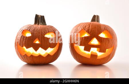 Two carved and illuminated halloween pumpkins prepared for the holiday reflected on white table and white isolated background. Stock Photo