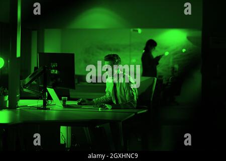 Young man working on computer at night in dark office. The designer works in the later time. Stock Photo