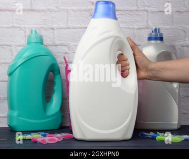 woman's hand holding a large white plastic bottle with detergent for washing clothes against a white brick wall background Stock Photo