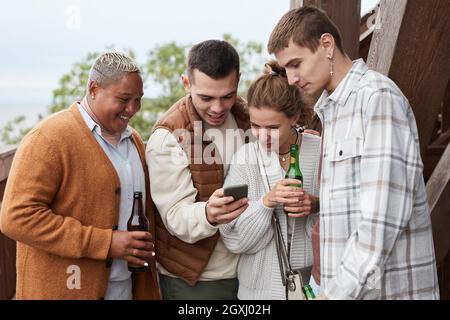 Diverse group young people using smartphone on balcony during party at lake house Stock Photo