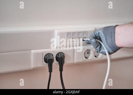 Connection to a computer network in the office, a gloved hand holds a cord for connecting to an Internet outlet Stock Photo