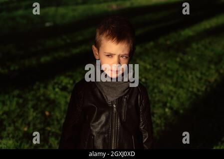 Emotive portrait of a stylish Caucasian boy wearing a black leather jacket. Outdoor portrait of cute little kid in the park on a nice autumn sunny day. Fashion boy Stock Photo