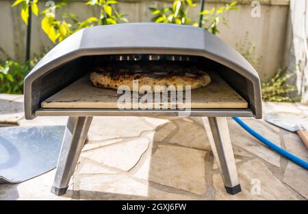 Making homemade pizza in portable high temperature gas pizza oven. Delicious pizza is baking in gas oven furnace for home made Neapolitan pizza. Speci Stock Photo