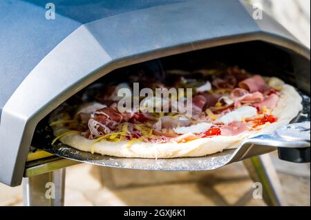 Making homemade pizza in portable high temperature gas pizza oven. Delicious pizza is baking in gas oven furnace for home made Neapolitan pizza. Speci Stock Photo