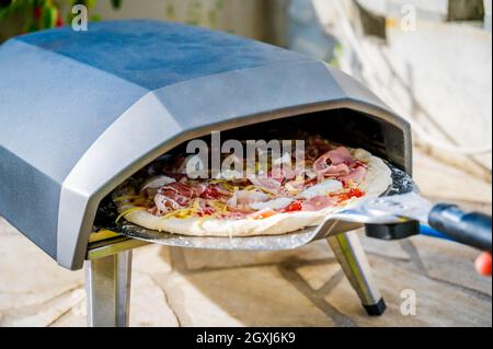 Making homemade pizza in portable high temperature gas pizza oven. Delicious pizza is baking in gas oven furnace for home made Neapolitan pizza. Speci Stock Photo