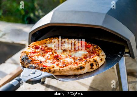 Making homemade pizza in portable high temperature gas pizza oven. Delicious pizza is baking in gas oven furnace for home made Neapolitan pizza. Speci Stock Photo