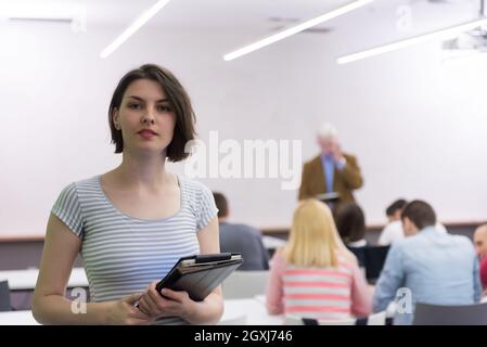 portrait of happy female student holding tablet while teacher teaching students in school classroom Stock Photo