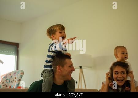 Two beautiful and happy parents are doing a piggyback ride to their children Stock Photo
