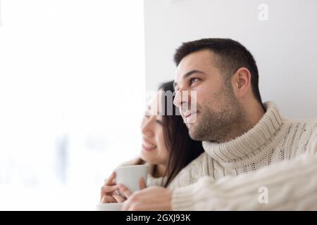 happy young multiethnic couple enjoying morning coffee by the window on cold winter day at home Stock Photo