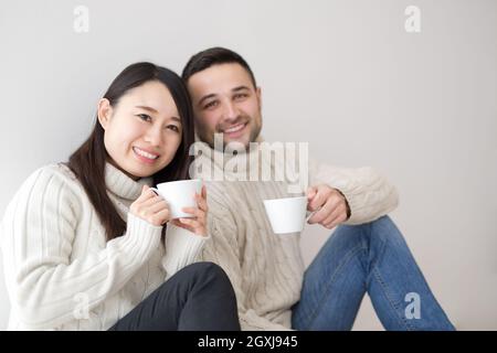 happy young multiethnic couple enjoying morning coffee by the window on cold winter day at home Stock Photo