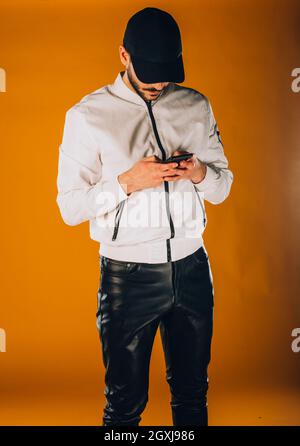 Stylish fashion guy posing against orange background using his mobile phone Stock Photo