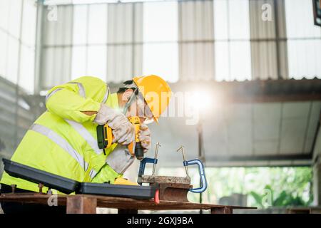 A worker is using an electric drill in an industrial plant. Stock Photo