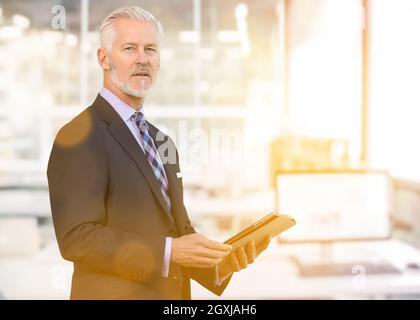 Portrait of senior businessman using tablet in front of his modern office with sun flares Stock Photo