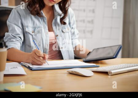 Close-up of office employee in casual wear sitting at table and analyzing data on tablet while preparing report in office Stock Photo