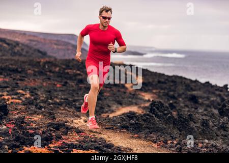 Mountain running ultra runner man athlete training cardio outdoor in extreme conditions on volcanic trail in coast landscape. Wet red rocks. Sports Stock Photo